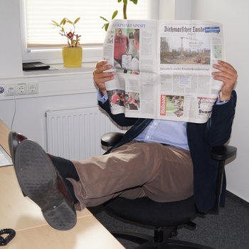 Mann liest Zeitung mit beiden Beiden auf dem Tisch